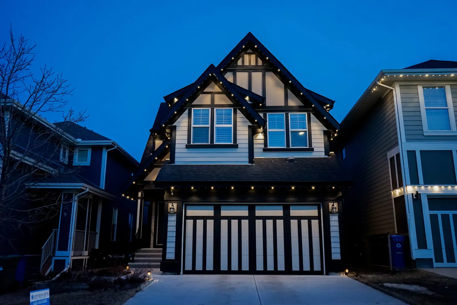 Tudor-style two-story home with warm white lights along every gable at dusk