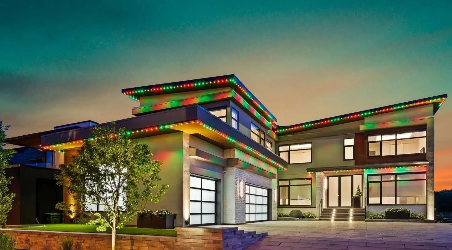 Modern home with red and green pattern lights along its flat rooflines at sunset