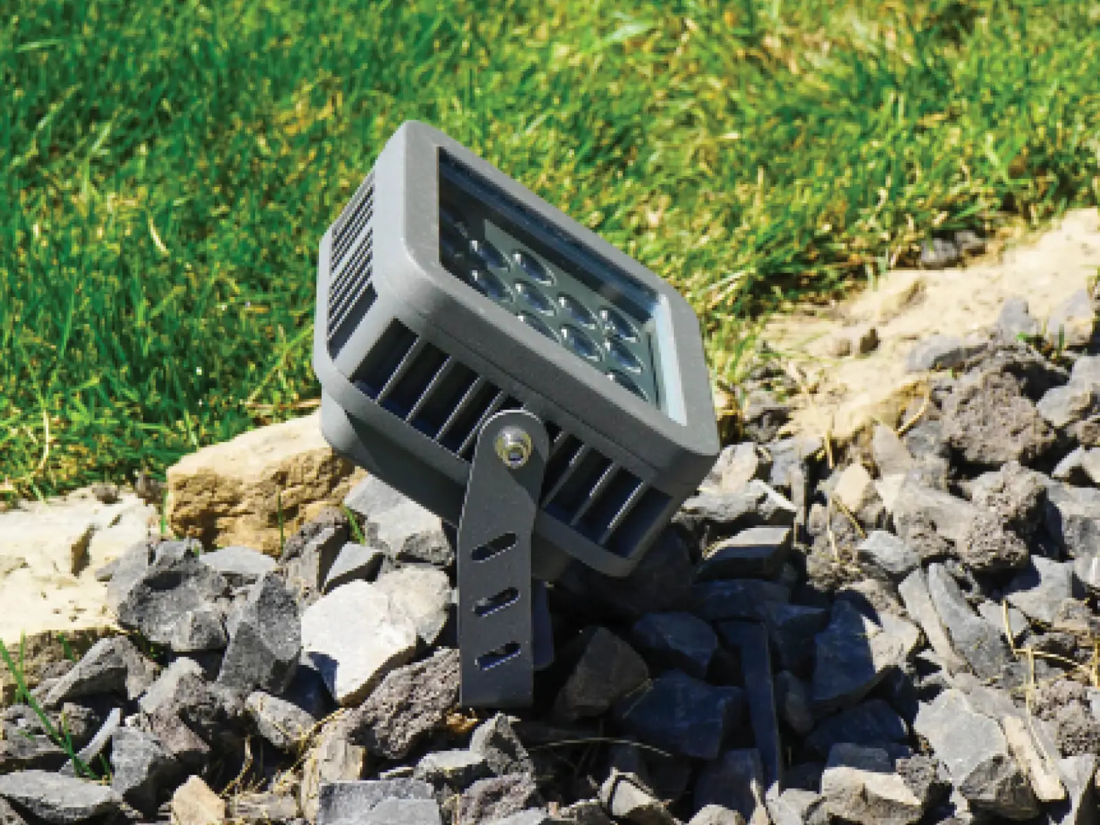 Gemstone landscape light fixture angled up from a rock bed beside a lawn