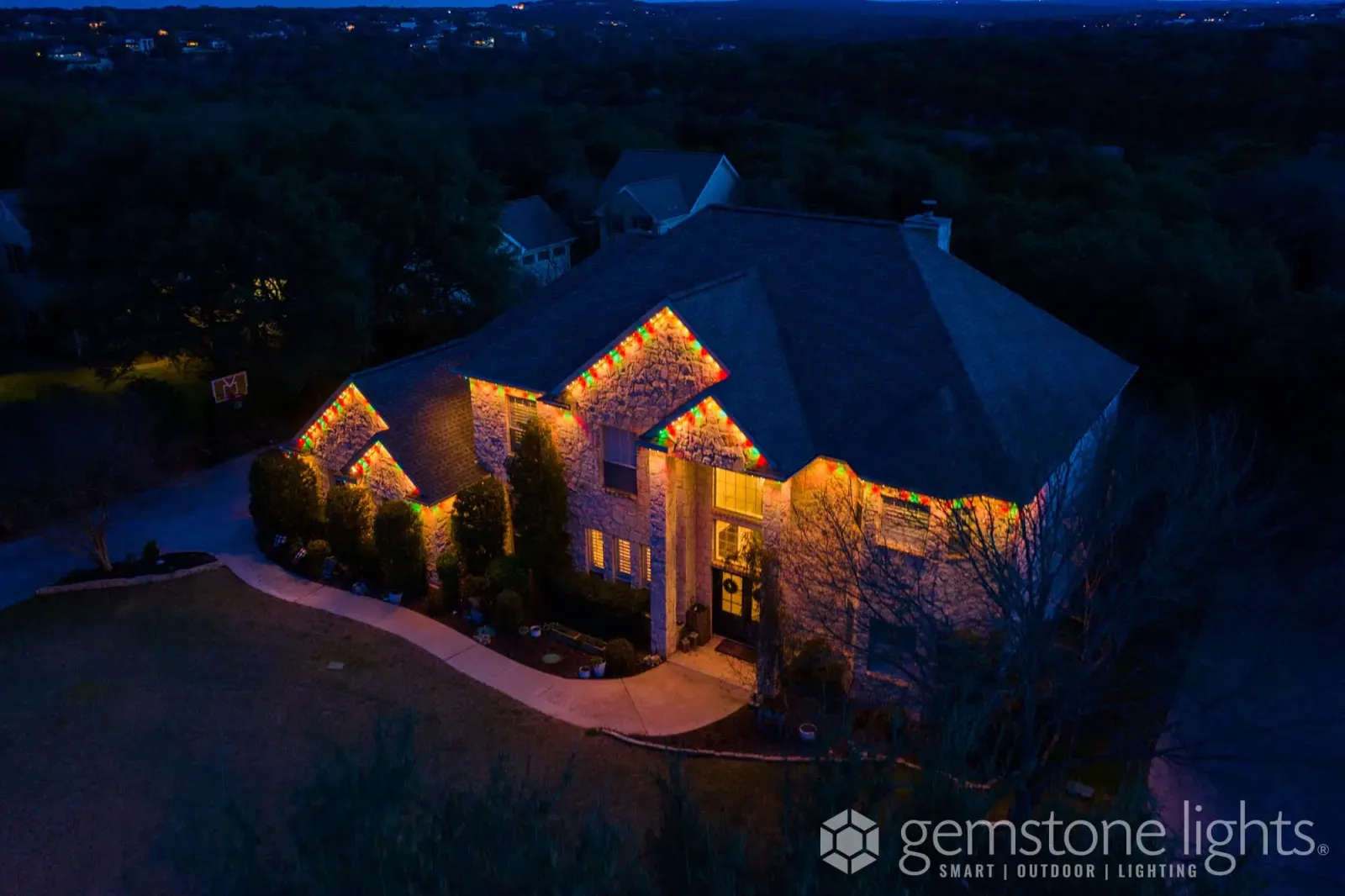 Aerial view of a wooded lot with a lit home