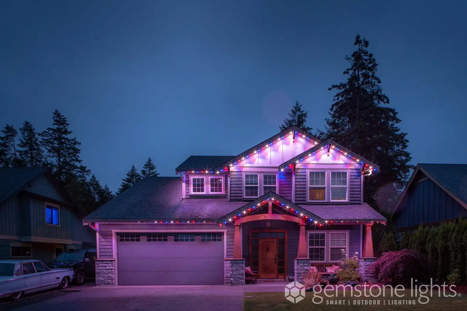 Craftsman-style home with porch columns and gables lit in purple and violet tones at dusk
