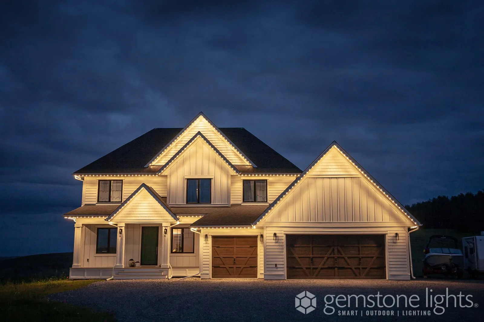 Farmhouse-style home with white board-and-batten gables outlined in warm white light