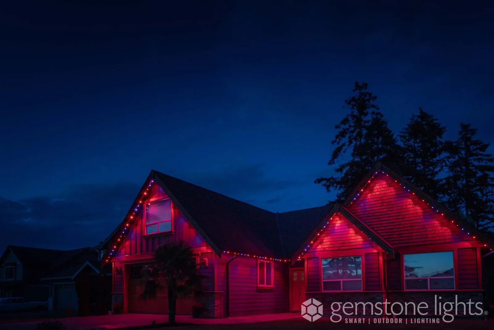 Single-story house with its eaves and gables outlined in bright red lights against a deep blue evening sky