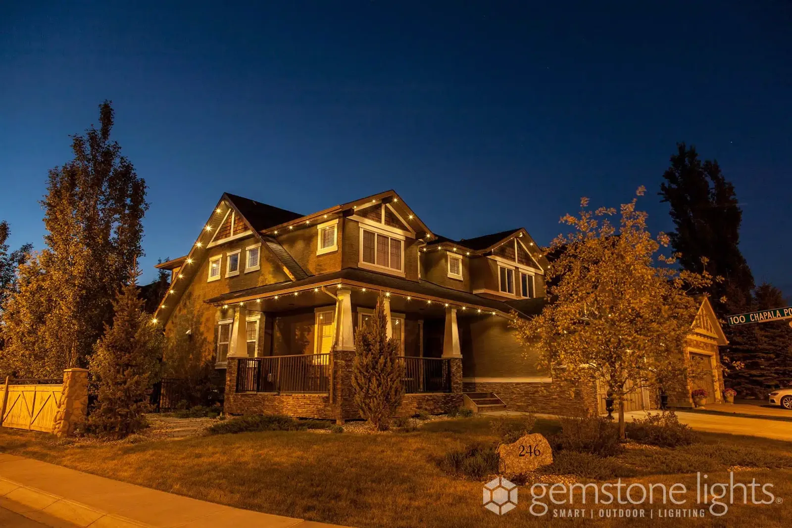 Craftsman house with stone columns and gables outlined in soft warm white lights at dusk