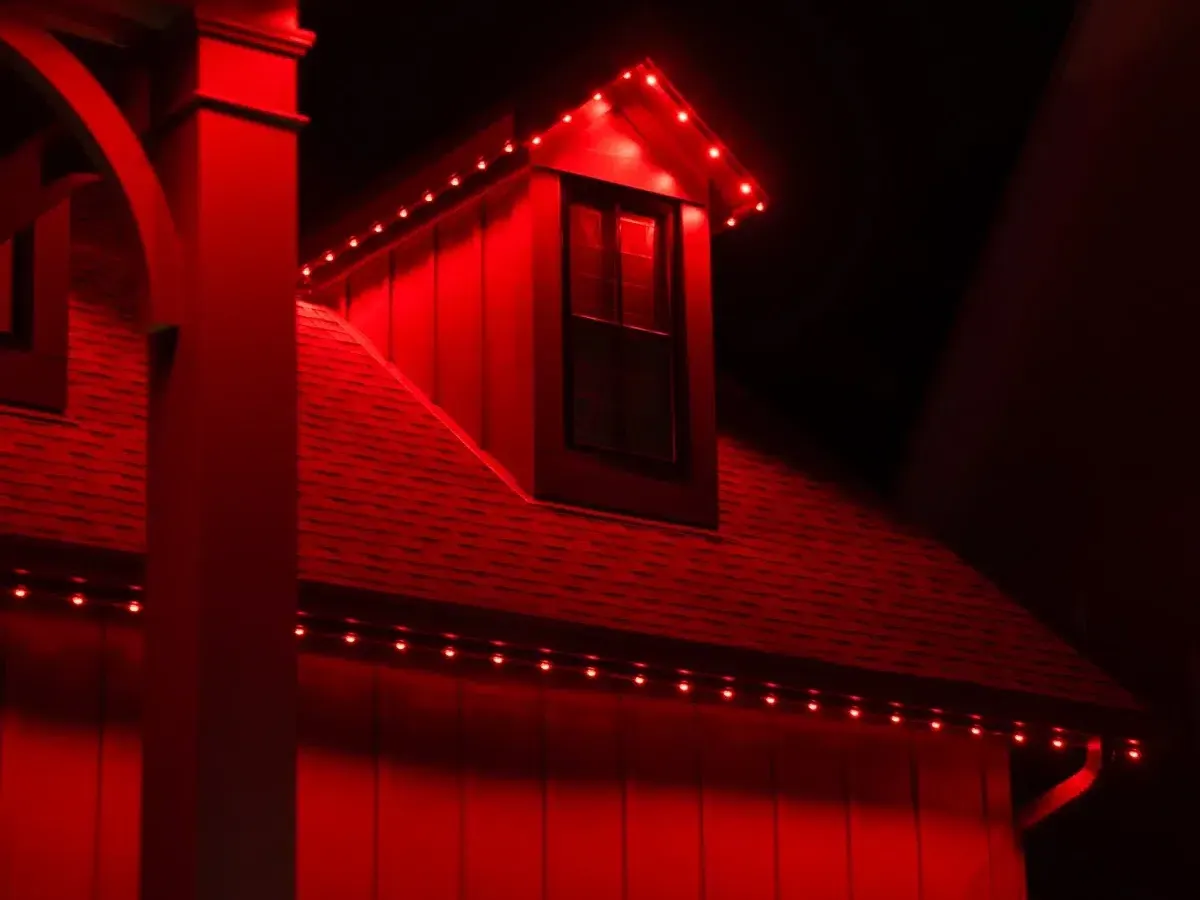 Close view of a house at night with roof, dormer and porch posts lit solid red