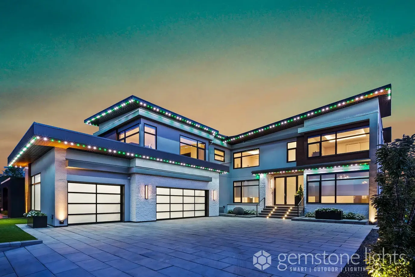 Large modern home at dusk with green, white and red lights along its flat rooflines
