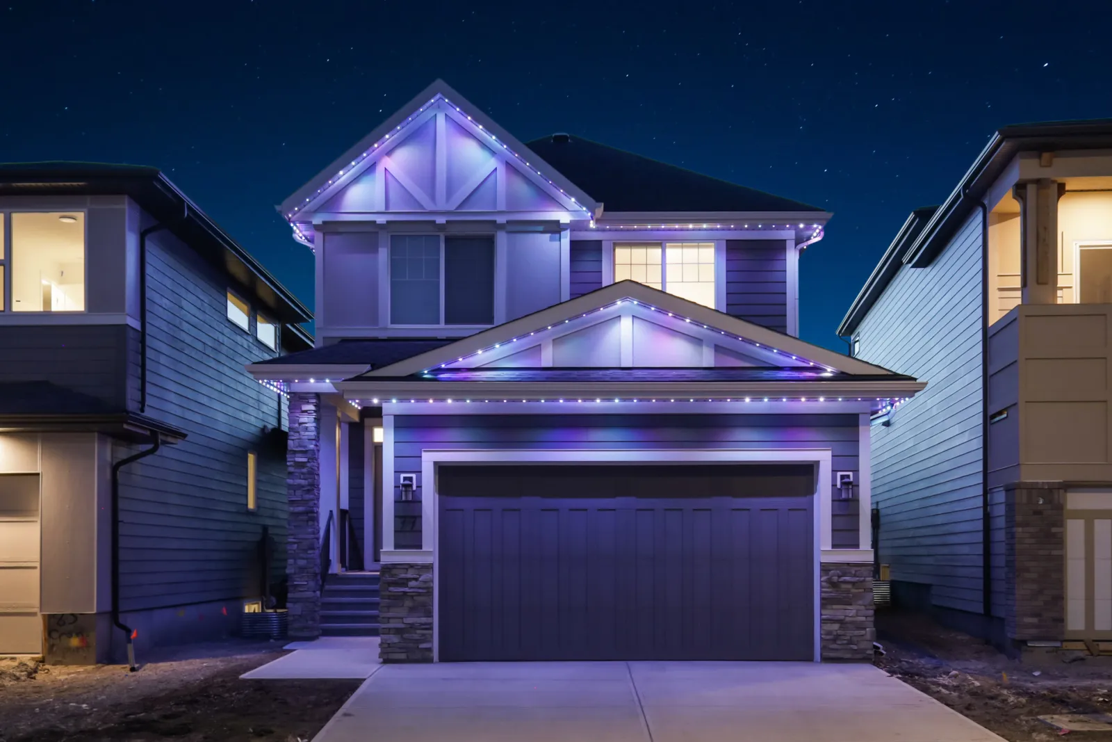 The same house at dusk with purple and white New Year's lights along every roofline
