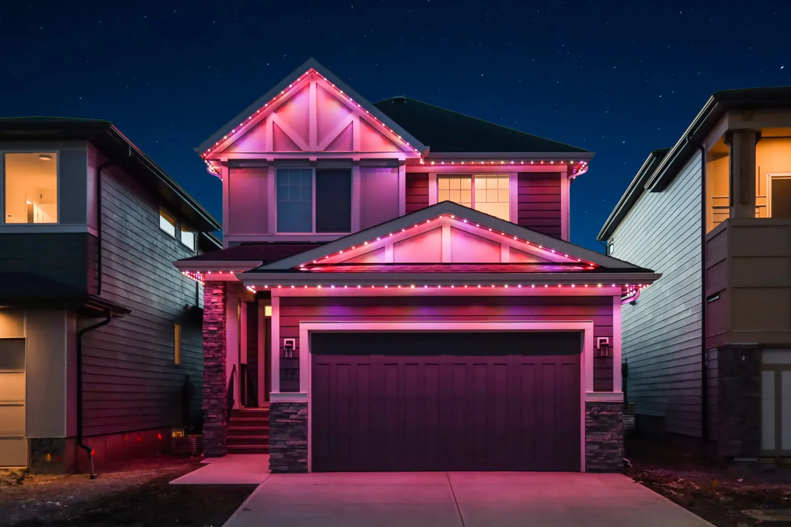 The same house at dusk with pink and red lights along every roofline