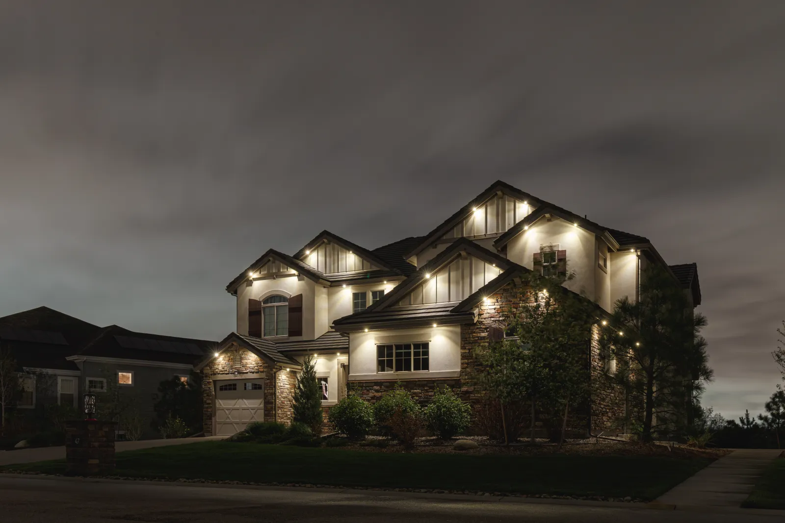 Large two-story home lit in warm white along its gables